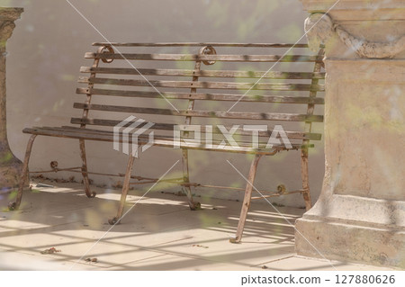 a weathered wooden bench and backrest supported by metal legs positioned between stone pedestal. a weathered wooden bench and backrest supported by metal legs positioned between stone pedestal. 127880626