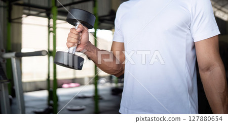 Focused Exercise. Young man lifting a dumbbell in gym for strength and fitness. 127880654