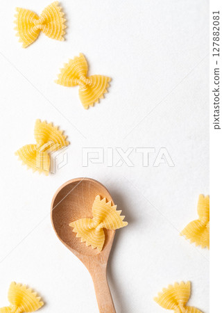 Flat lay of raw farfalle pasta on a wooden spoon placed on a white background, Bow-tie shaped pasta 127882081