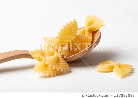 Raw farfalle pasta on a wooden spoon placed on a white background, Bow-tie shaped pasta  127882082
