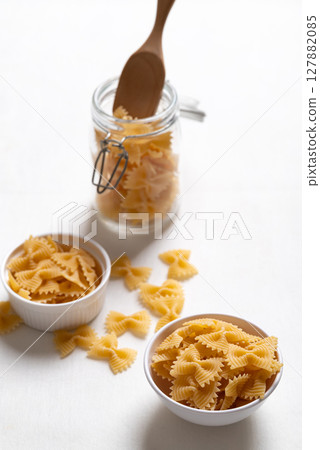Raw farfalle pasta in a white bowl and glass jar on white background, Bow-tie shaped pasta Raw farfalle pasta in a white bowl and glass jar on white background, Bow-tie shaped pasta 127882085