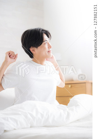 A young man waking up in bed bathed in the morning sun stretching his arms, close-up 127882151