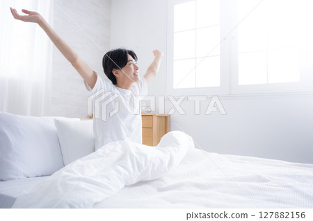 一位年輕男子在床上醒來,沐浴在清晨的陽光下,伸展雙臂,以萬歲姿勢仰望 一位年輕男子在床上醒來,沐浴在清晨的陽光下,伸展雙臂,以萬歲姿勢仰望 127882156