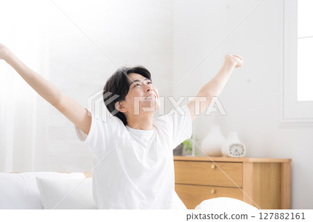 一位年輕男子在床上醒來，沐浴在清晨的陽光下，伸展雙臂，以萬歲姿勢仰望 127882161