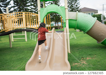 Child Playing Joyfully on Playground Slide Surrounded by Green Grass and Trees in a Bright Sunny Day, Elevating Outdoor Play Experience Child Playing Joyfully on Playground Slide Surrounded by Green Grass and Trees in a Bright Sunny Day, Elevating Outdoor Play Experience 127882385