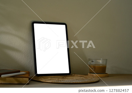 Digital tablet with blank screen on wooden table next to books with soft shadows 127882457