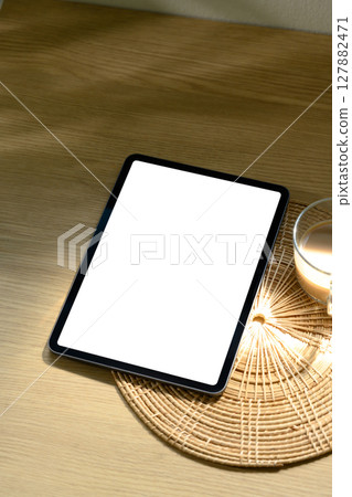 Digital tablet with blank white screen on a rattan coaster with warm light Digital tablet with blank white screen on a rattan coaster with warm light 127882471