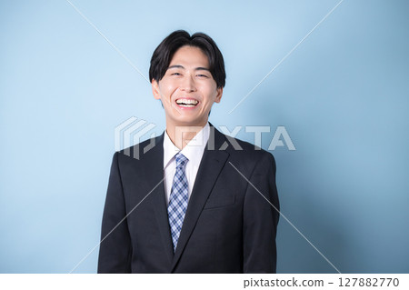 一位年輕的商人穿著西裝看著鏡頭,淺藍色,令人耳目一新的形象 一位年輕的商人穿著西裝看著鏡頭,淺藍色,令人耳目一新的形象 127882770