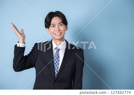 穿著西裝的年輕商人看著相機,淺藍色背景,清爽的微笑形象,推薦或指導 穿著西裝的年輕商人看著相機,淺藍色背景,清爽的微笑形象,推薦或指導 127882774