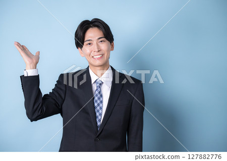穿著西裝的年輕商人看著相機，淺藍色背景，清爽的微笑形象，推薦或指導 127882776