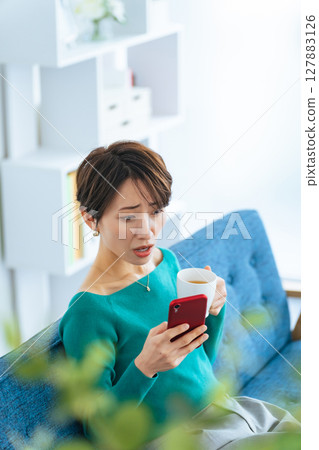 中年婦女在現代客廳裡對自己的智慧型手機感到驚訝 127883126