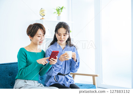 Two women looking at a smartphone in a modern living room 127883132