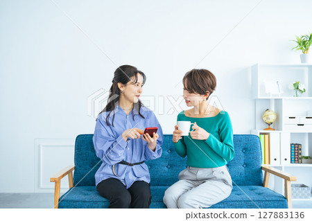 Two women looking at a smartphone in a modern living room 127883136