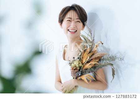一位身穿白色洋裝的女子手捧一束乾燥花 127883172