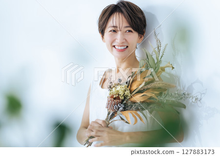 A woman in a white dress holding a bouquet of dried flowers A woman in a white dress holding a bouquet of dried flowers 127883173