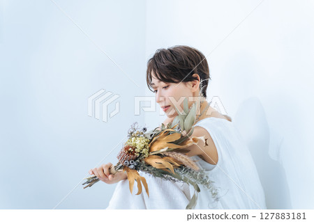 A woman in a white dress holding a bouquet of dried flowers 127883181