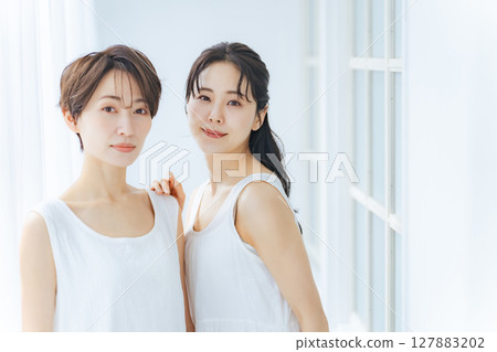 兩位身穿白色連身裙的女士在明亮的房間裡緊緊地站在一起 127883202