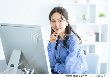 一位女士在現代辦公室裡一邊工作一邊看著電腦顯示器 127883240