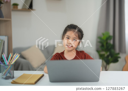 Smiling young girl using laptop at home for online learning, study, and education in cozy living room with natural light and comfortable atmosphere Smiling young girl using laptop at home for online learning, study, and education in cozy living room with natural light and comfortable atmosphere 127883267