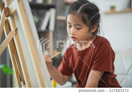 Young girl focused on painting at home, creative expression through art, childhood exploration, indoor activity, artistic development, talent realization 127883272