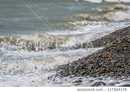 Sea water splashing over the stones on the beach 127884376