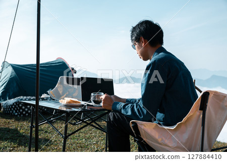 Remote work technology online close up communication smart phone laptop telephone digital travel brown nature sunlight camp beverage morning sit drink coffee tent orange outlying concept background. 127884410