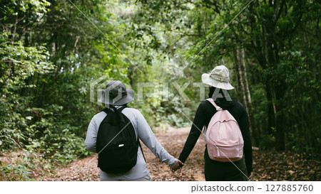 Two female friends with backpacks on vacation hiking through countryside together. Asian friend girls backpacker friend travel in forest wild together. happy and enjoying sunny day while hiking. Two female friends with backpacks on vacation hiking through countryside together. Asian friend girls backpacker friend travel in forest wild together. happy and enjoying sunny day while hiking. 127885760