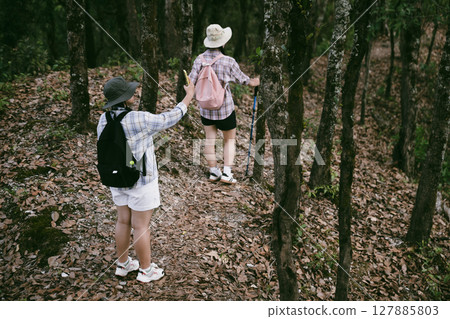 Two female friends with backpacks on vacation hiking through countryside together. Asian friend girls backpacker friend travel in forest wild together. happy and enjoying sunny day while hiking. 127885803