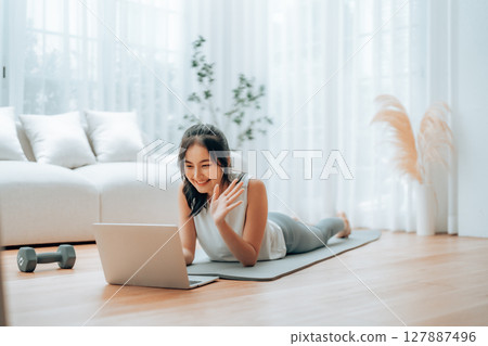 Young Asian woman lying on the floor on yoga mat in front of laptop and training at home 127887496