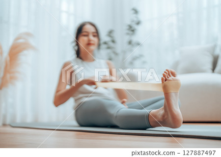 Young Asian woman doing pilates workout using elastic strap pulling with arms 127887497