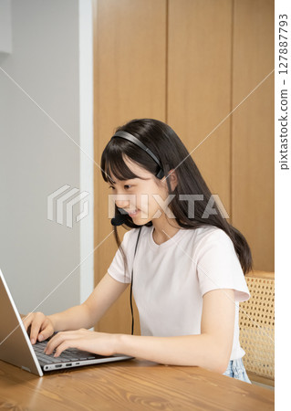 A girl wearing a headset and operating a computer A girl wearing a headset and operating a computer 127887793