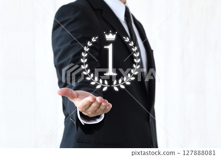 A businessman holding up the number 1 surrounded by a laurel wreath - an image of number one in the rankings 127888081
