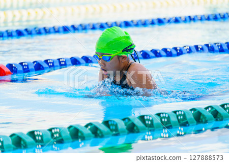 Swimmer child swims breaststroke swimming style in a race swimming pool. Water sports and competition, learning to swim classes for children. 127888573