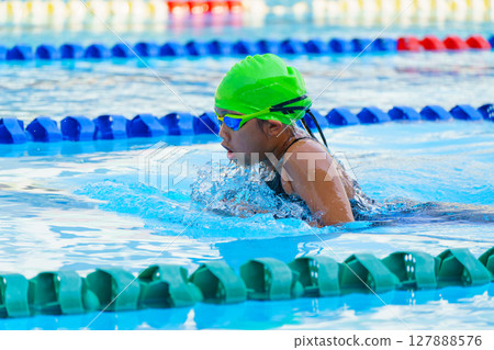 Swimmer child swims breaststroke swimming style in a race swimming pool. Water sports and competition, learning to swim classes for children. 127888576