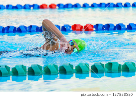 Swimmer child swims freestyle swimming style in a race swimming pool. Water sports and competition, learning to swim classes for children. 127888580