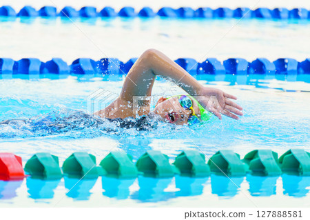 Swimmer child swims freestyle swimming style in a race swimming pool. Water sports and competition, learning to swim classes for children. 127888581