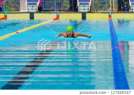 Swimmer child swims butterfly swimming style in a race swimming pool. Water sports and competition, learning to swim classes for children. Swimmer child swims butterfly swimming style in a race swimming pool. Water sports and competition, learning to swim classes for children. 127888587