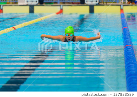 Swimmer child swims butterfly swimming style in a race swimming pool. Water sports and competition, learning to swim classes for children. 127888589
