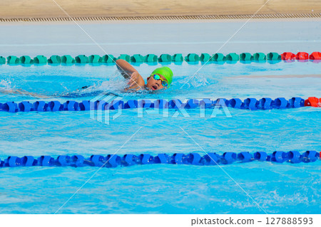 Swimmer child swims freestyle swimming style in a race swimming pool. Water sports and competition, learning to swim classes for children. 127888593