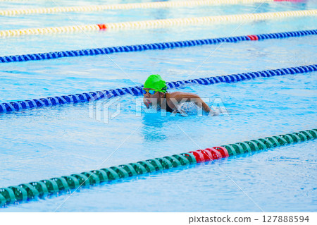 Swimmer child swims butterfly swimming style in a race swimming pool. Water sports and competition, learning to swim classes for children. 127888594