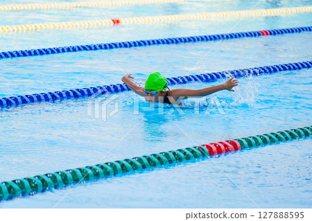 Swimmer child swims butterfly swimming style in a race swimming pool. Water sports and competition, learning to swim classes for children. Swimmer child swims butterfly swimming style in a race swimming pool. Water sports and competition, learning to swim classes for children. 127888595