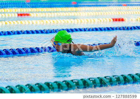 Swimmer child swims butterfly swimming style in a race swimming pool. Water sports and competition, learning to swim classes for children. Swimmer child swims butterfly swimming style in a race swimming pool. Water sports and competition, learning to swim classes for children. 127888599