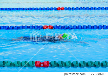 Swimmer child swims backstroke swimming style in a race swimming pool. Water sports and competition, learning to swim classes for children. Swimmer child swims backstroke swimming style in a race swimming pool. Water sports and competition, learning to swim classes for children. 127888600