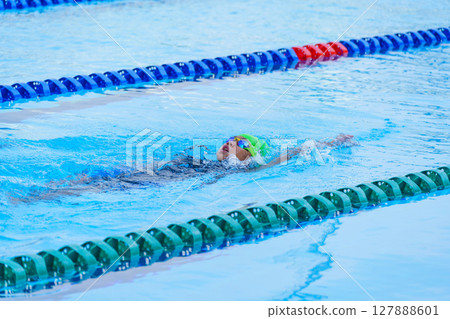 Swimmer child swims backstroke swimming style in a race swimming pool. Water sports and competition, learning to swim classes for children. Swimmer child swims backstroke swimming style in a race swimming pool. Water sports and competition, learning to swim classes for children. 127888601