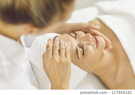 Close up photo of pretty young woman lying with closed eyes and having face or head massage in spa Close up photo of pretty young woman lying with closed eyes and having face or head massage in spa 127889182