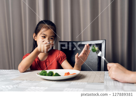 Little cute kid girl refusing to eat healthy vegetables. Children do not like to eat vegetables. Little cute kid girl refusing to eat healthy vegetables. Children do not like to eat vegetables. 127889381