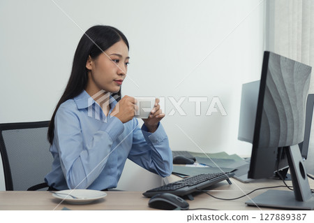 Asian woman was drinking coffee in the early morning while contemplating the program and code on the computer screen. 127889387