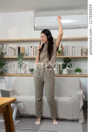 Energetic Dance and Music Enjoyment. Young woman expressing joy while singing at home. Energetic Dance and Music Enjoyment. Young woman expressing joy while singing at home. 127889824