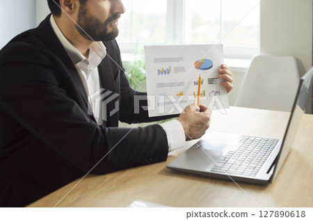 Businessman working in office showing finance stat at laptop monitor screen having video call Businessman working in office showing finance stat at laptop monitor screen having video call 127890618