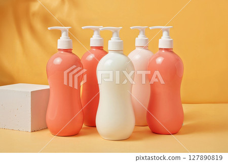 Five pump bottles, in shades of peach and white, arranged on an orange background with soft shadows. Ideal for cosmetic, beauty, or skincare product mockups. Five pump bottles, in shades of peach and white, arranged on an orange background with soft shadows. Ideal for cosmetic, beauty, or skincare product mockups. 127890819